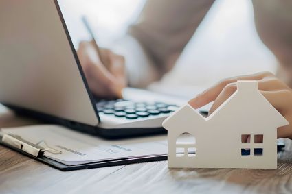 Foto: Person bearbeitet Akten, Modell eines Hauses im Vordergrund